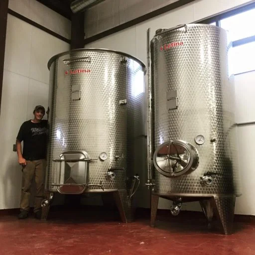 Man standing next to two stainless steel wine tanks in Liquid Art Winery in Kansas, USA.